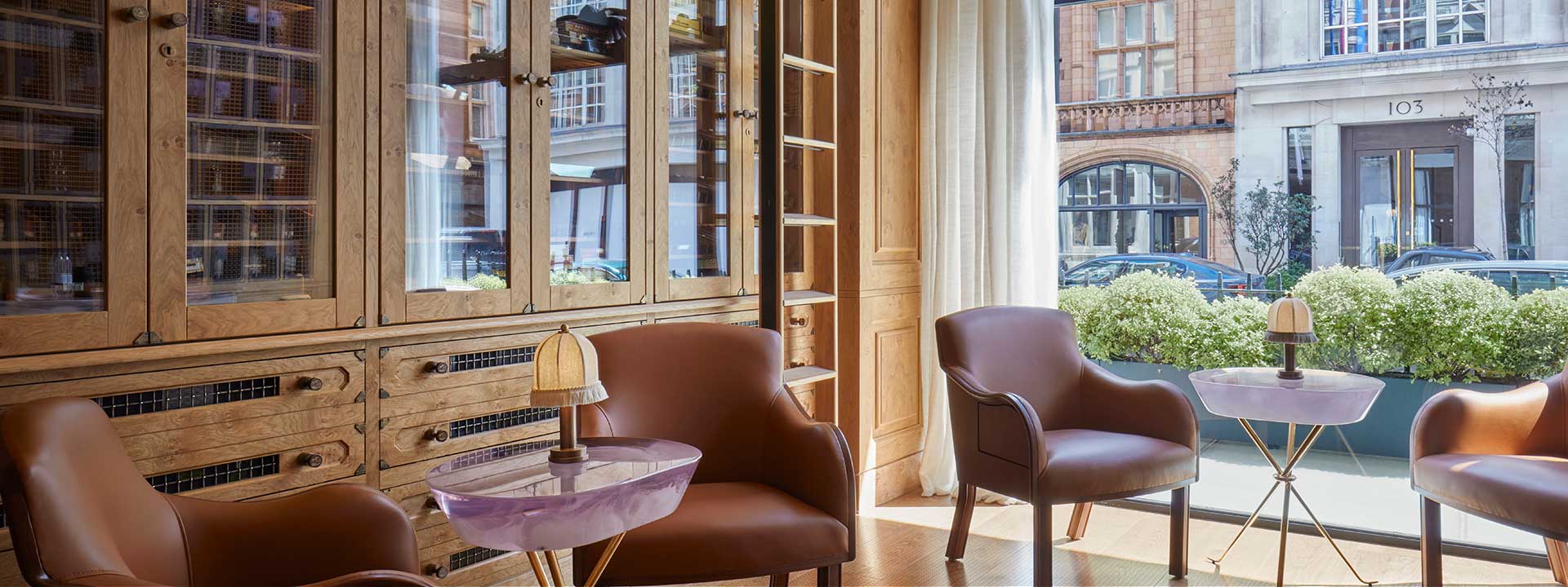 The Connaught Cigar Merchants - view of armchairs around small tables in front of a cupboard with glass doors containing the cigar collection, and with a view onto a street in London out the window