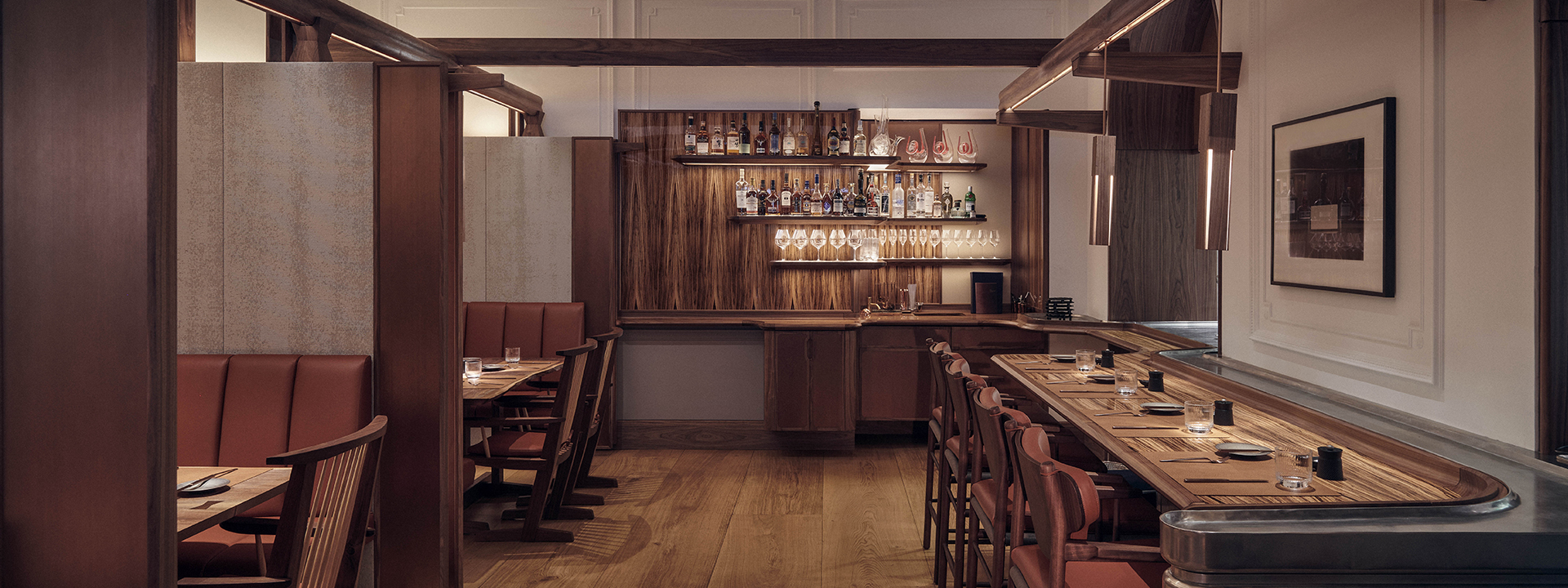 The Connaught Grill room with counter table with bar stools on the right-hand side, shelves with alcohol against a wall in the middle, and table with chairs in the left-hand side.